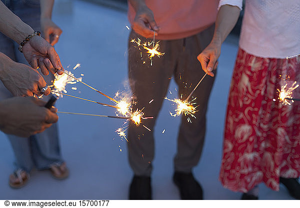 Group of young men and women with sparklers on a rooftop in an urban setting.