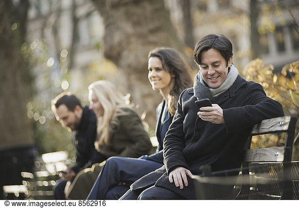 Group on bench in urban park using smartphones