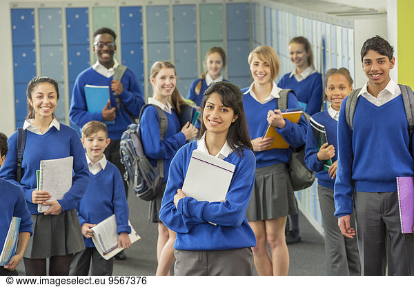 Group portrait of schoolchildren wearing school uniforms standing in corridor and smiling