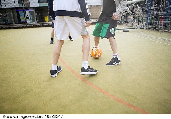 Gruppe von Erwachsenen die Fußball auf dem städtischen Fußballplatz spielen niedriger Abschnitt