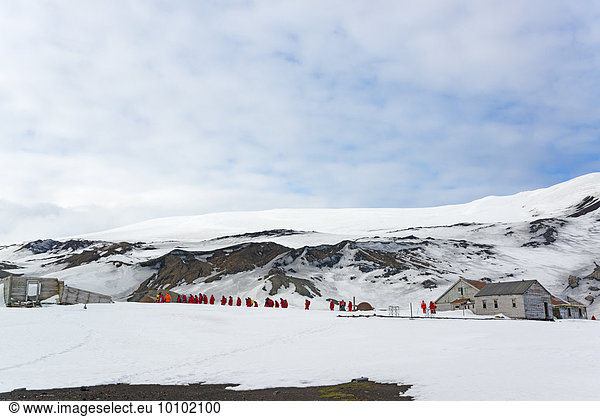 Gruppe von Menschen in der Nähe einer Basis auf Deception Island  im Hintergrund schneebedeckte Berge.