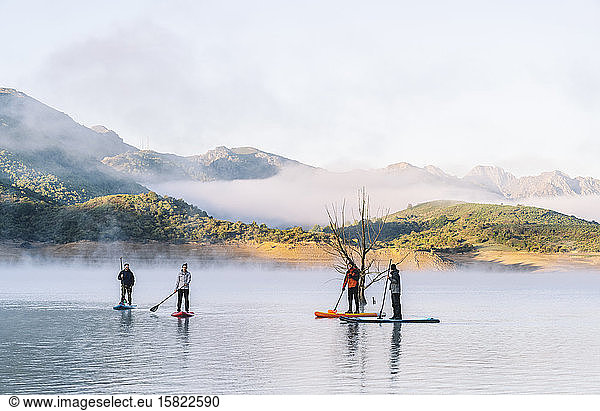 Gruppe von Menschen steht auf Paddel-Surfen auf einem See im Nebel