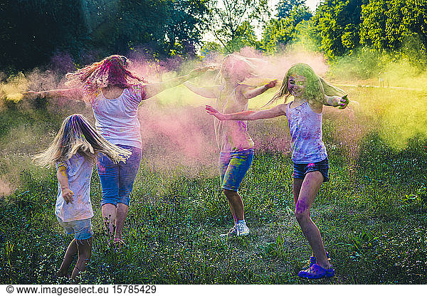 Gruppe von zwei Frauen und zwei Mädchen feiern das Fest der Farben auf einer Wiese