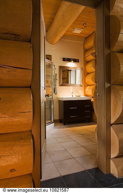Guest bathroom with glass shower stall and wooden vanity inside a Scandinavian cottage style log home