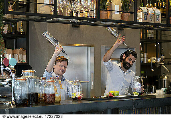 Gut aussehender Barkeeper und Auszubildender gießen Alkohol in ein Fruchtglas am Bartresen