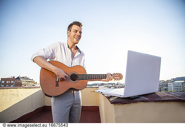 gut aussehender junger Sänger  der während der Quarantäne vom Dach seines Hauses aus für seine Fans in den sozialen Medien auftritt