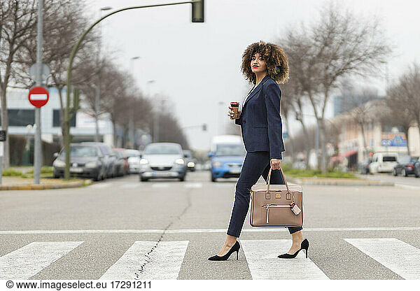 Gut gekleidete Geschäftsfrau mit Handtasche beim Überqueren der Straße in der Stadt