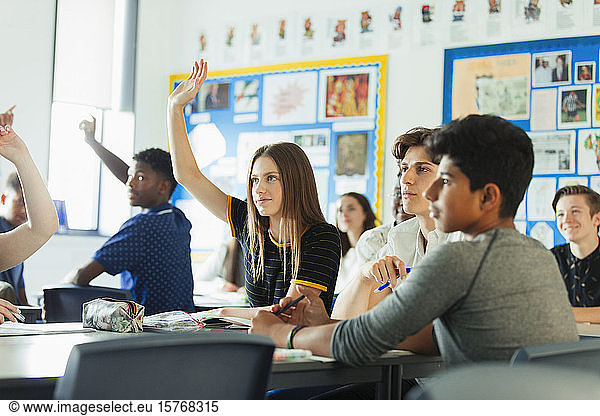 Gymnasiasten mit erhobenen Händen  die während des Unterrichts im Klassenzimmer Fragen stellen
