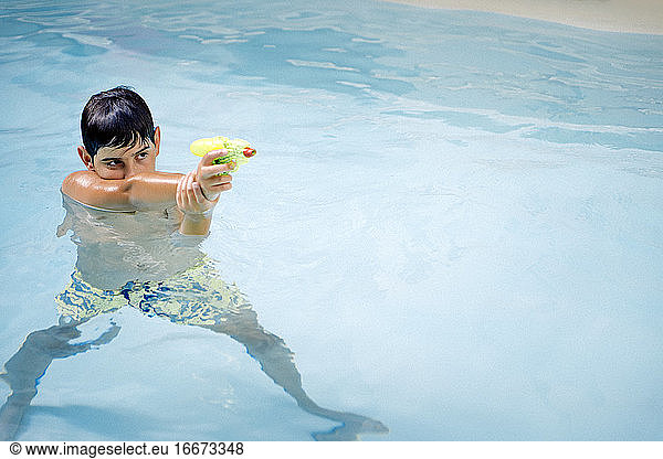 Hübscher  dunkelhaariger Junge  der mit einer Wasserpistole im Wasser des Pools spielt
