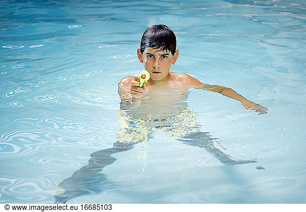 Hübscher  dunkelhaariger Junge  der mit einer Wasserpistole im Wasser des Pools spielt