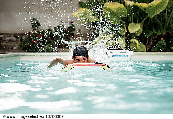 Hübscher dunkelhaariger Junge spielt mit einem Body Surf Board im Pool