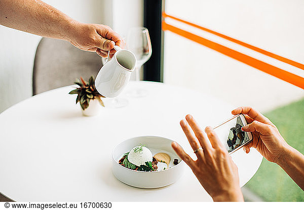 Hände  die mit dem Smartphone Fotos vom Essen machen  während der Kellner das Essen serviert