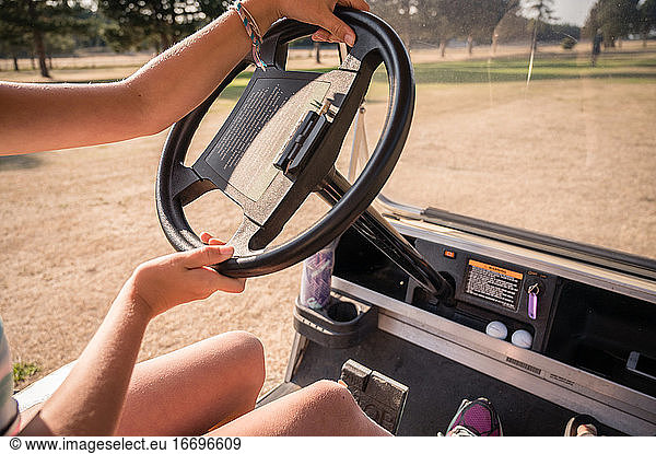 Hände eines jungen Mädchens am Lenkrad eines Golfwagens