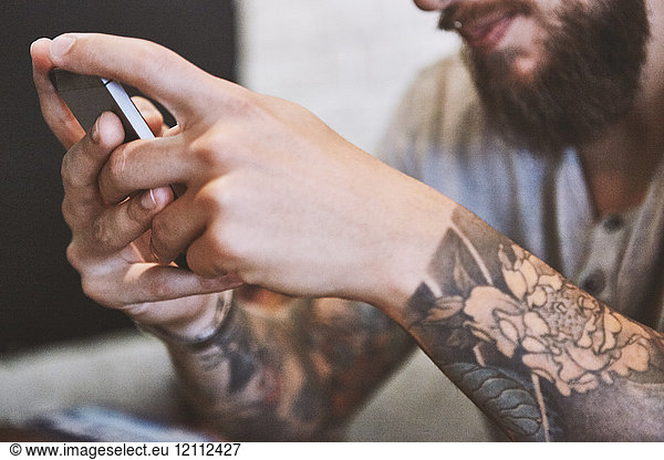 Hände eines tätowierten jungen männlichen Hipsters  der ein Smartphone hält  Nahaufnahme