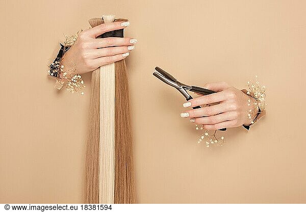 Hände mit Blumen halten Haarsträhnen für Verlängerungen auf einem beigen Hintergrund. hair beauty