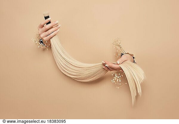 Hände mit Blumen halten Haarsträhnen für Verlängerungen auf einem beigen Hintergrund. hair beauty