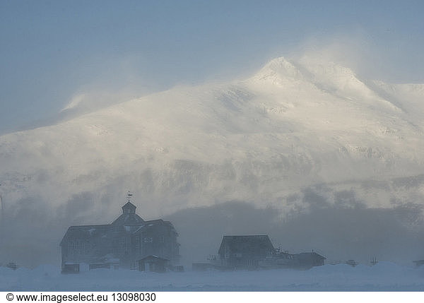 Häuser gegen schneebedeckte Berge bei nebligem Wetter