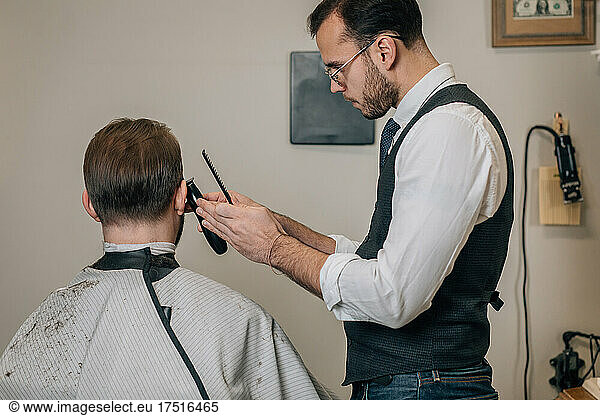 Hairdresser barber cuts hair with trimer.