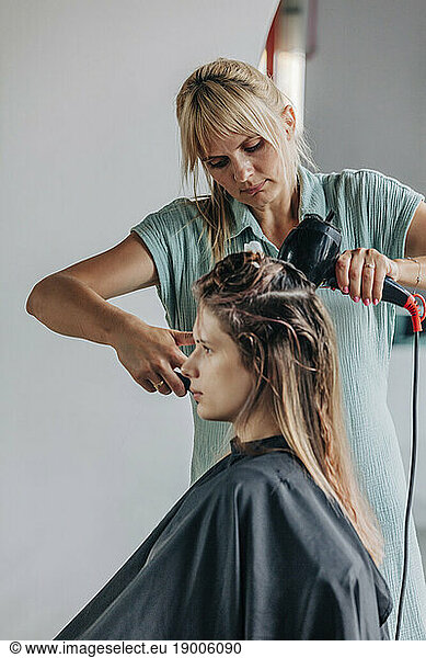 Hairdresser blow drying client's hair in salon