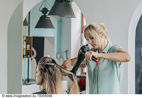 Hairdresser blow drying young client's hair in salon