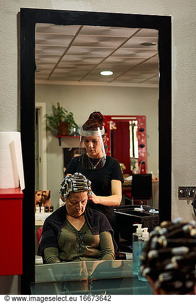 Hairdresser combs a client with a face shield in her salon