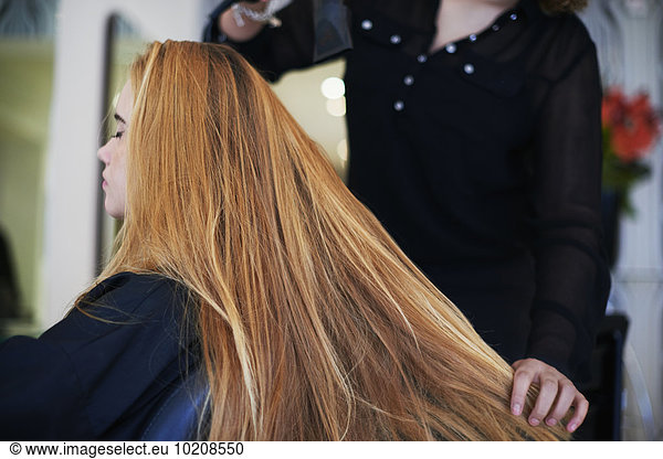 Hairdresser drying customer’s long hair in salon