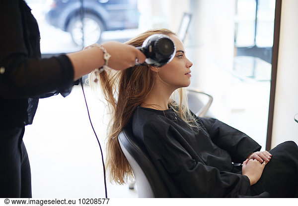 Hairdresser drying customer’s long hair in salon