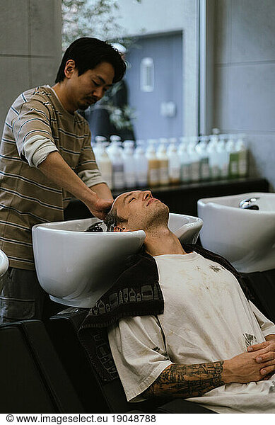 Hairstylist washing hair to handsome man in beauty salon.