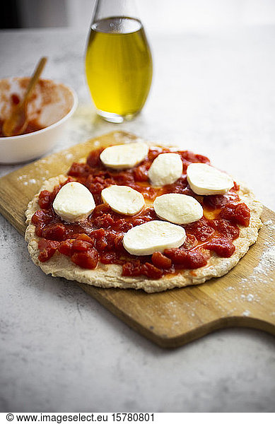 Half-made Margharita pizza on cutting board