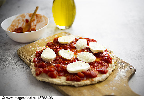 Half-made Margharita pizza on cutting board