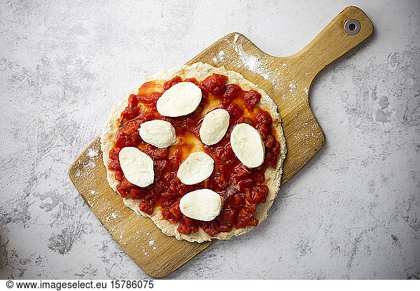 Half-made Margharita pizza on cutting board