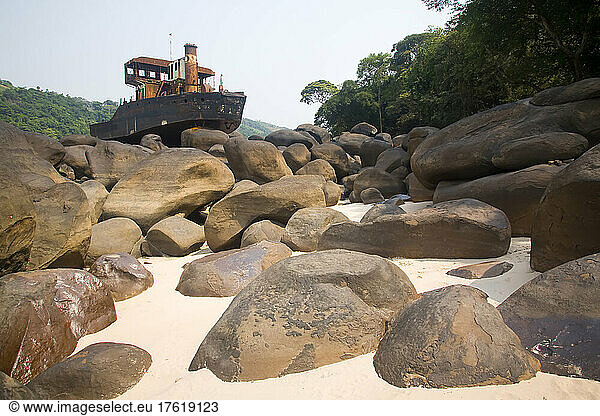 Half of a large cargo vessel sits on a pile of boulders.; Congo River  Democratic Republic of the Congo.