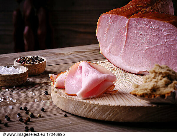 Ham on wooden board with salt and pepper in bowls  bread and rosemary