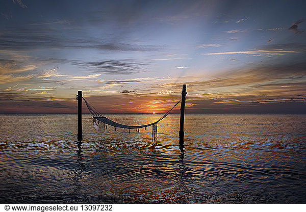Hammock tied to wooden poles on sea during sunset