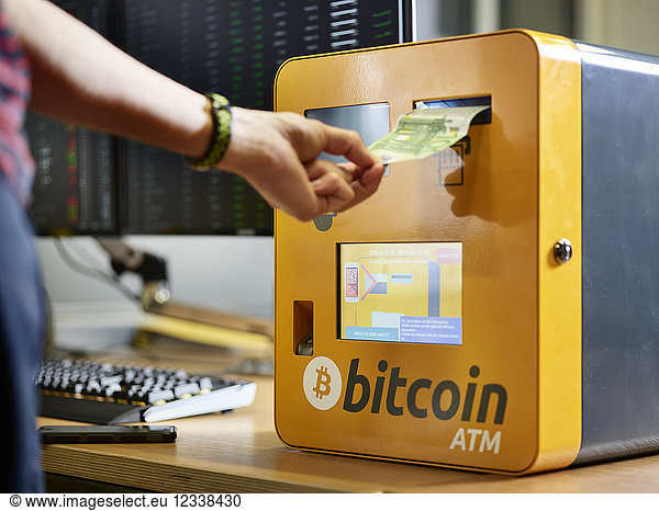 Hand  die einen 100-Euro-Schein in einen Bitcoin-Automaten steckt