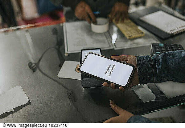 Hand einer Frau beim kontaktlosen Bezahlen mit dem Smartphone in einer Werkstatt