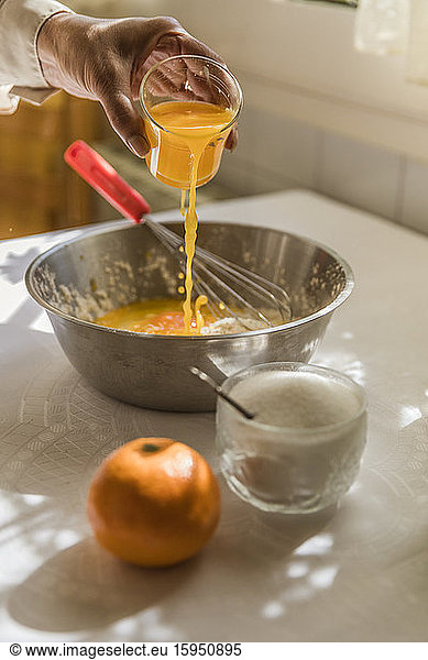 Hand einer Frau gießt Orangensaft in Schüssel