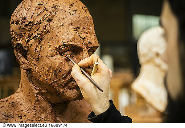 Hand eines Bildhauers  der ein Auge eines Tonkopfes fertigstellt