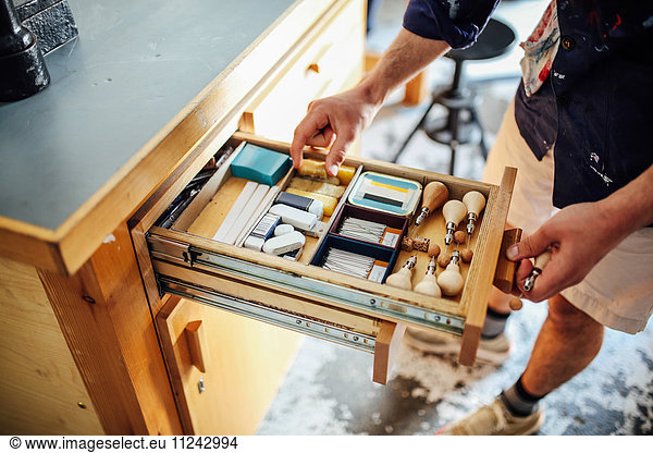 Hand greift in offene Schublade mit Geräten und Materialien in Buchkunstwerkstatt