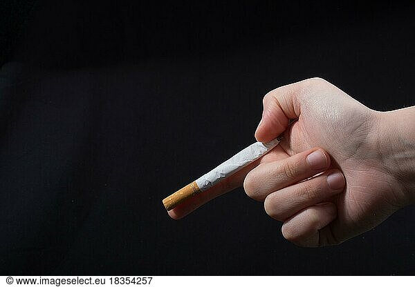 Hand hält eine Zigarette wie Waffe auf schwarzem Hintergrund