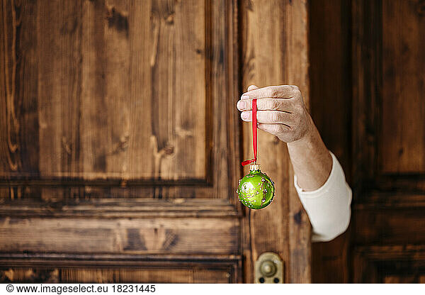 Hand holding green Christmas bauble in front of wooden door