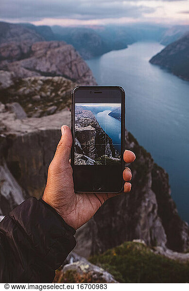 Hand holding smartphone with image of scene in background on it at Norwegian Fjords.