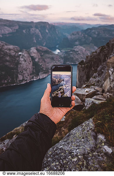 Hand holding smartphone with image of scene in background on it at Norwegian Fjords