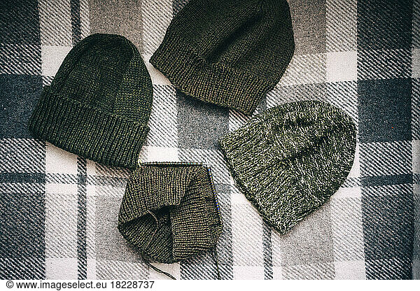 hand-knitted hats of various shades of green on a checkered plaid