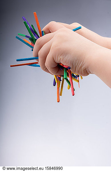 Hand letting coloured wooden sticks drop on white