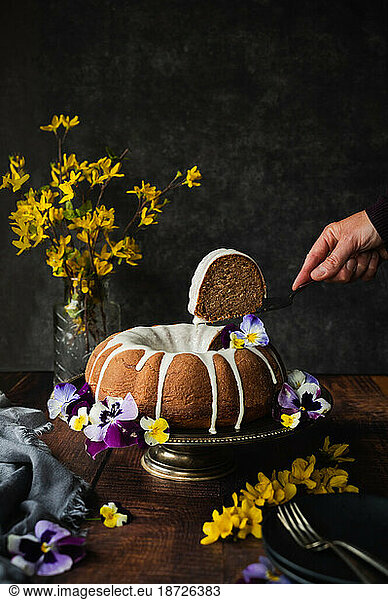 Hand lifting a piece of bundt cake decorated with flowers.