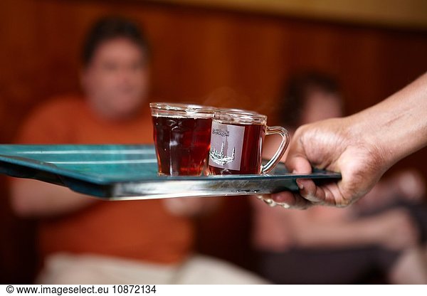 Hand mit Tablett mit Tassen mit Morgentee im Café  Muscat  Oman  Naher Osten