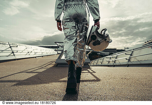 Hand of astronaut holding space helmet walking on footpath