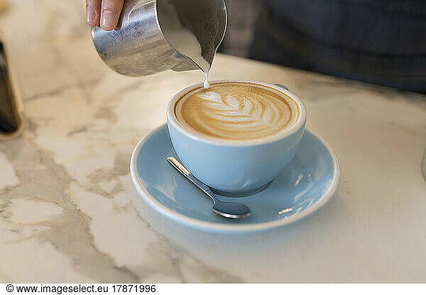 Hand of barista making froth art in coffee cup