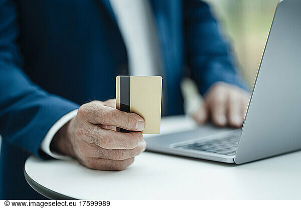 Hand of businessman holding credit card using laptop on table at office